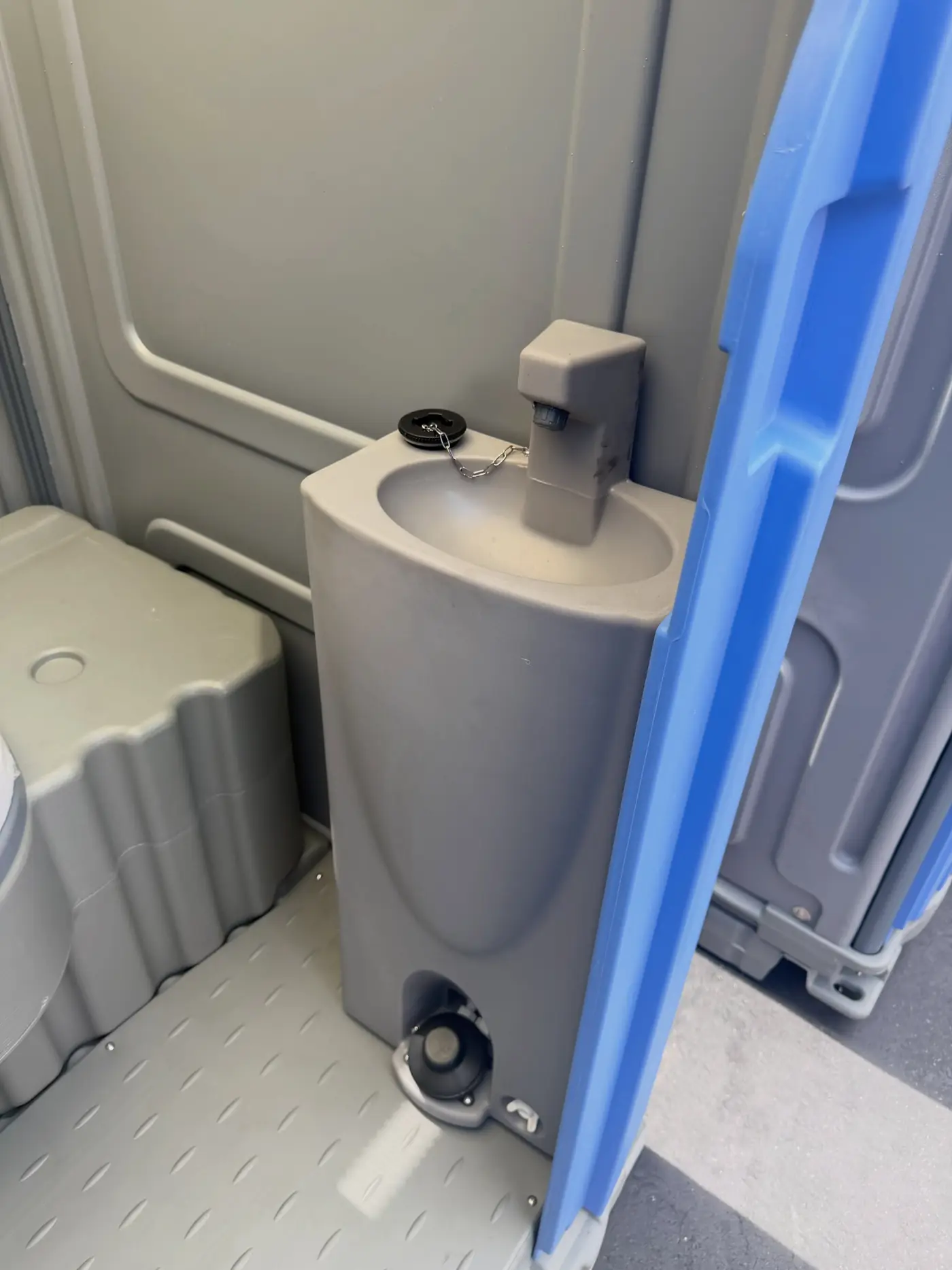 Corner of a deluxe porta potty interior showing the hand wash basin and dispenser