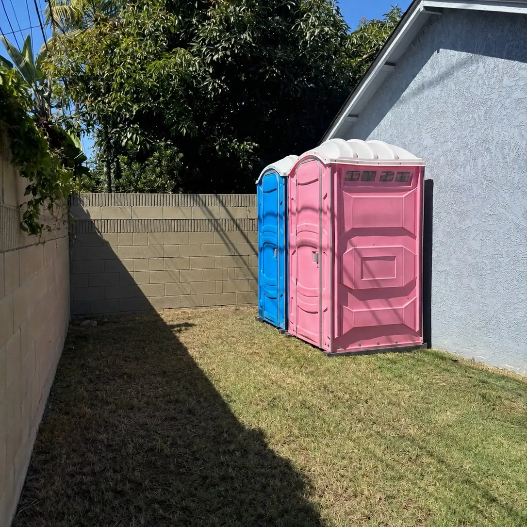 Pink event porta potty beside a house on a lawn