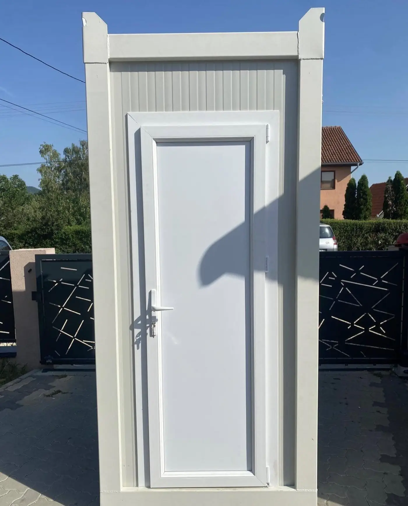 White flushable porta potty cabin with a solid door set on pavers outside a home