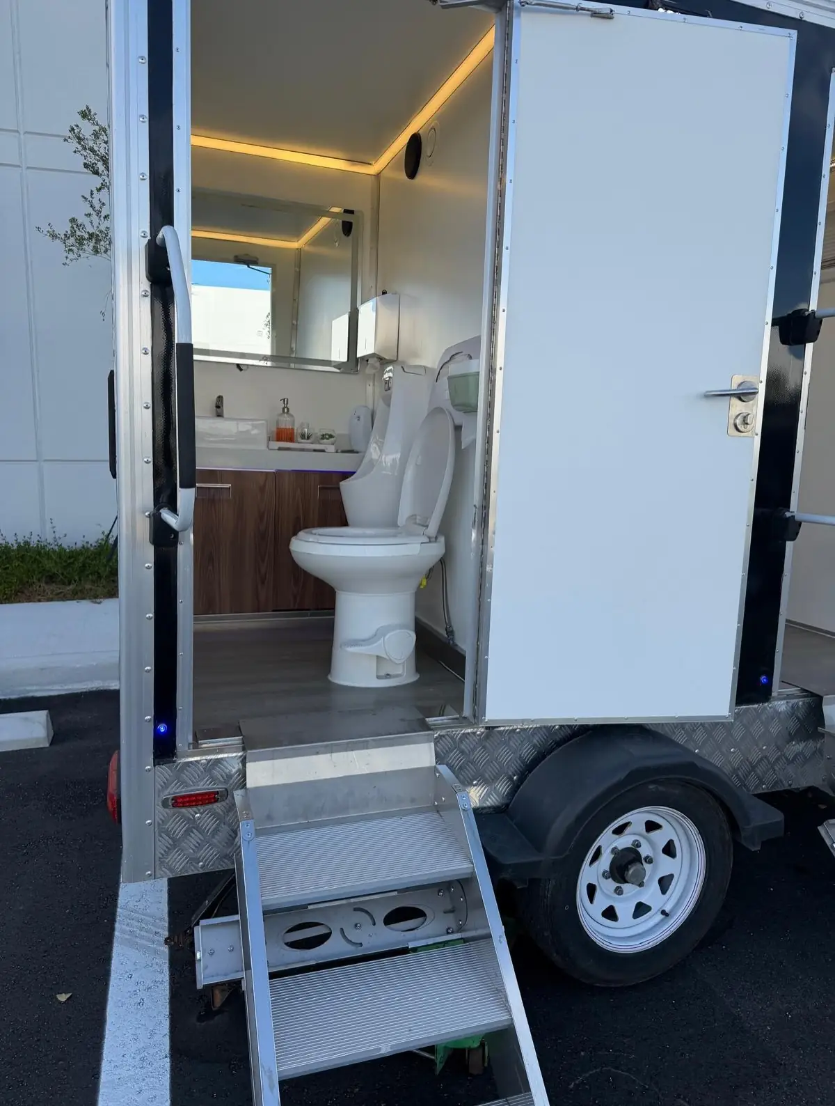 Open door of a restroom trailer showing the entry steps, toilet and lit interior