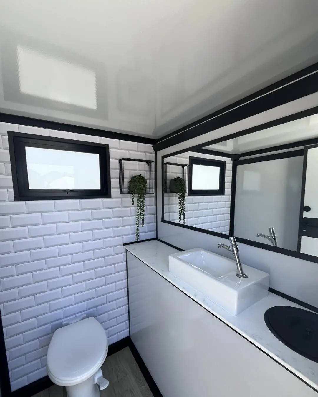 White tiled restroom trailer interior with a vessel sink, mirror and toilet