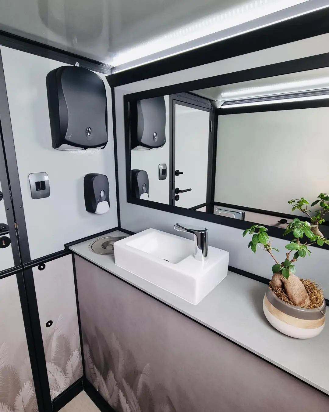 Restroom trailer vanity with white vessel sink, mirror and small plant
