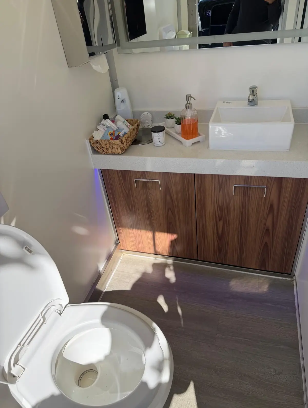Restroom trailer interior with wood-cabinet vanity, white sink and large mirror