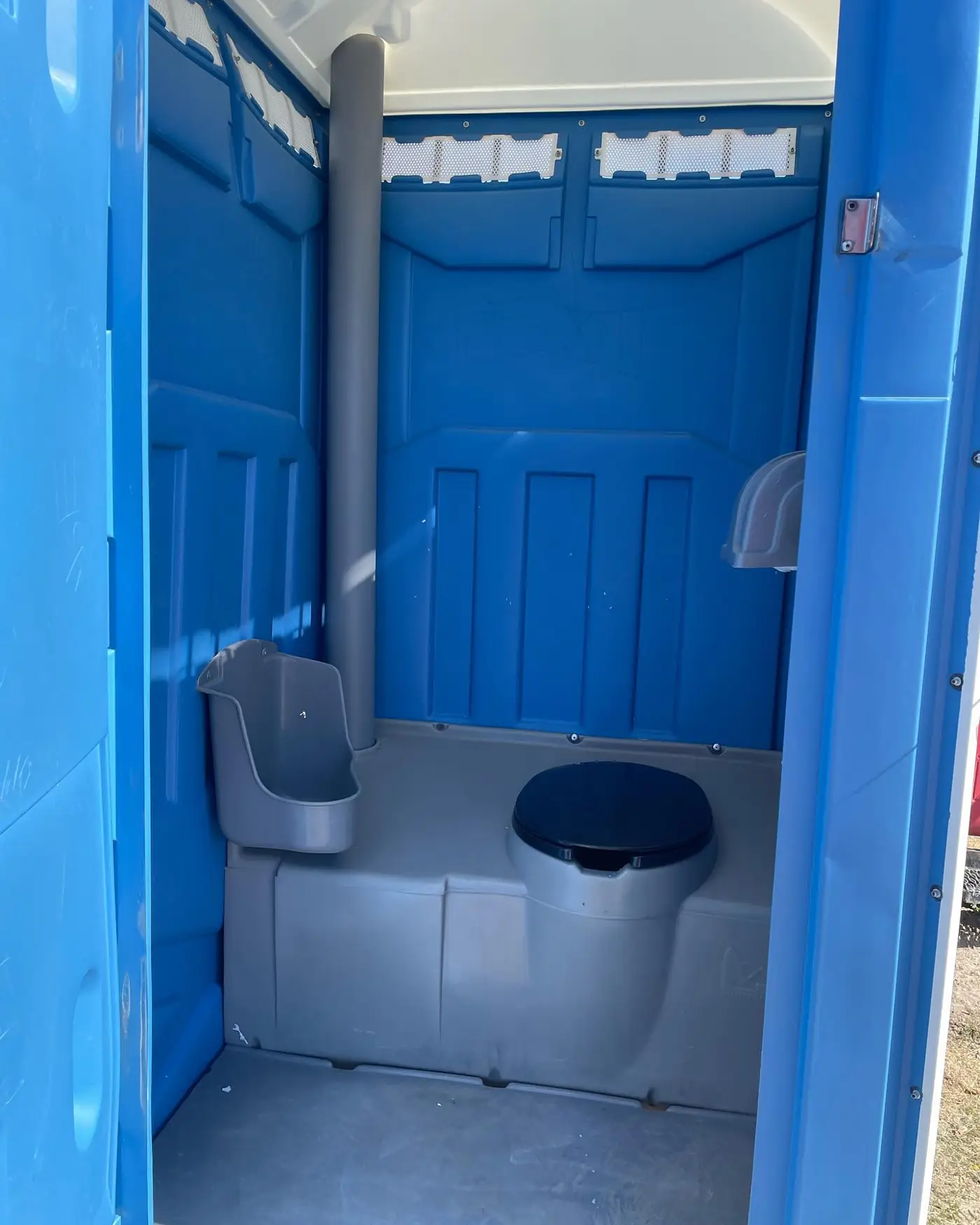 Interior of a blue standard porta potty showing the toilet seat, urinal and toilet paper holder